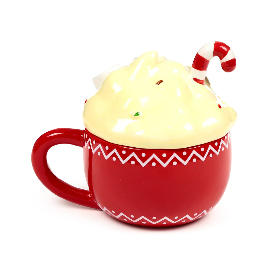 Angled view of a red ceramic mug with a white zigzag and dot pattern. It features a cream-coloured lid styled like whipped cream, adorned with small sprinkles and a red and white striped candy cane decoration.