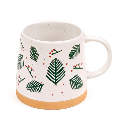 Angled view of a white speckled stoneware mug with a green pine sprigs and red berries design, featuring a natural light brown unglazed base.