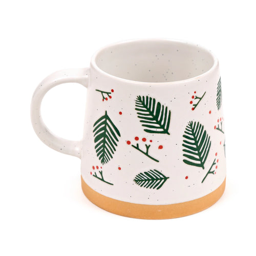 Angled view of a white speckled stoneware mug, decorated with green pine sprigs and red berries. It features an unglazed light brown base and a visible handle on the left.