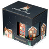Angled view of a Christmas Village porcelain mug in its dark blue packaging. The box has a cut-out window, revealing the mug's festive design of colourful snow-covered houses and trees. The packaging itself features a winter village illustration and the text 'PORCELAIN MUG'.