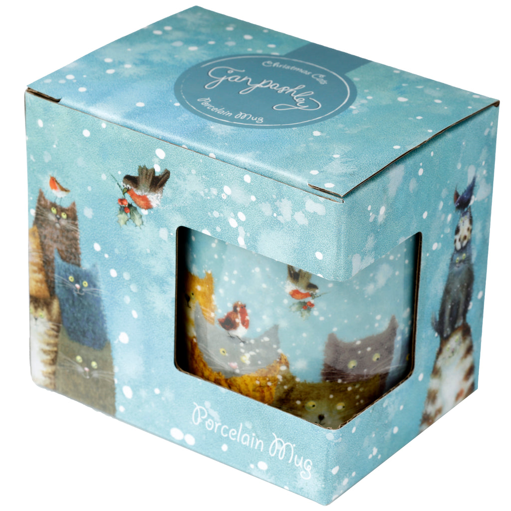 Angled view of a Jan Pashley Christmas Cats porcelain mug in its light blue gift box. The box features a snowy design and an oval label, with a window revealing the mug's artwork depicting cats, robins, and holly on a winter scene.