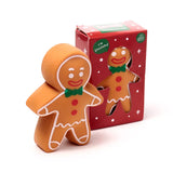 Front angled view of a brown stretchy gingerbread man fidget toy with white icing, red buttons, and a green bow tie, standing next to its red Christmas-themed box featuring a window showing another gingerbread man toy.