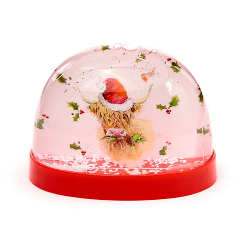 Christmas snow globe with a Highland Coo wearing a red Father Christmas hat, surrounded by holly leaves, red berries, and a robin, suspended in pinkish liquid with white glitter, on a red base.