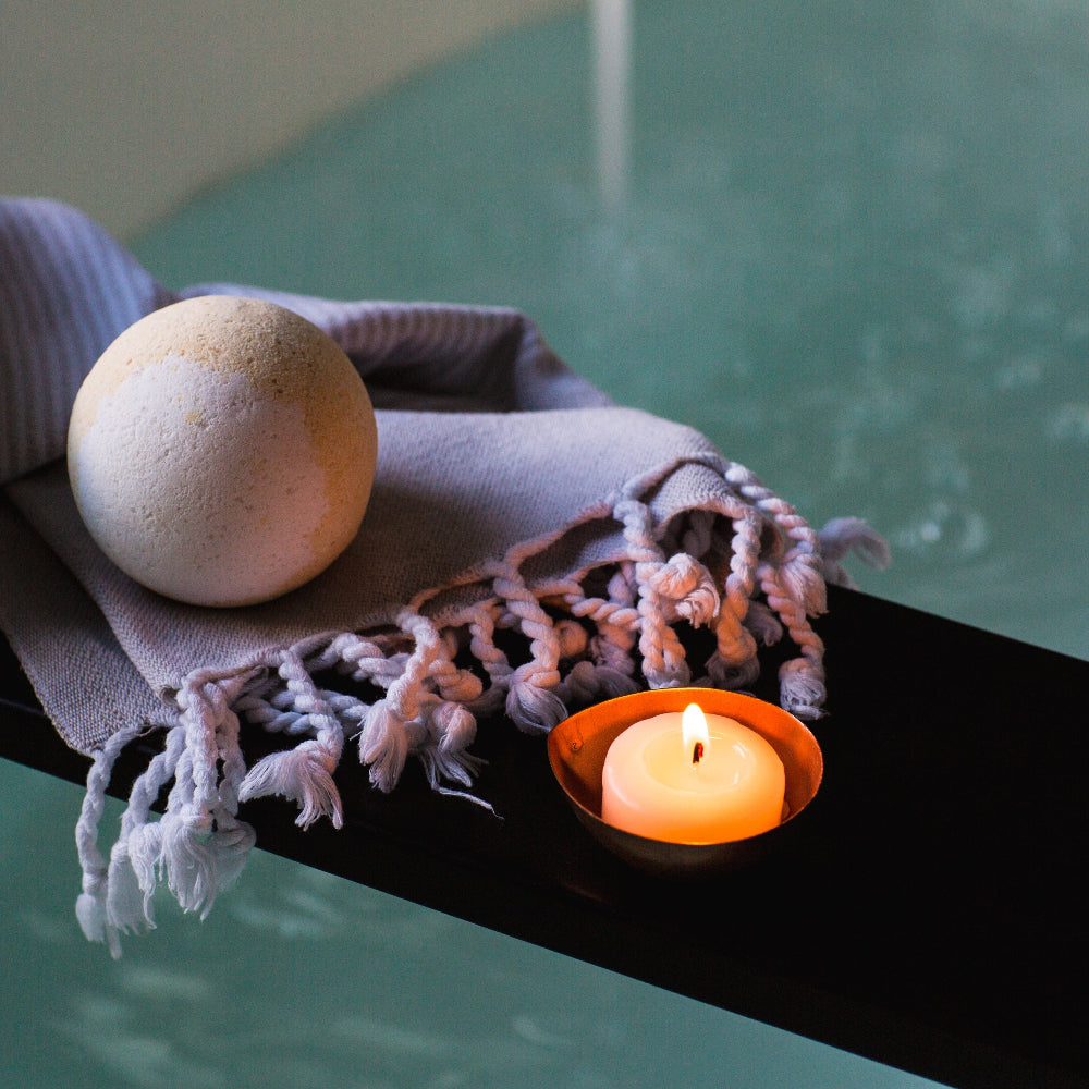 Candle, bath bomb, and towel on a ledge with water in the background