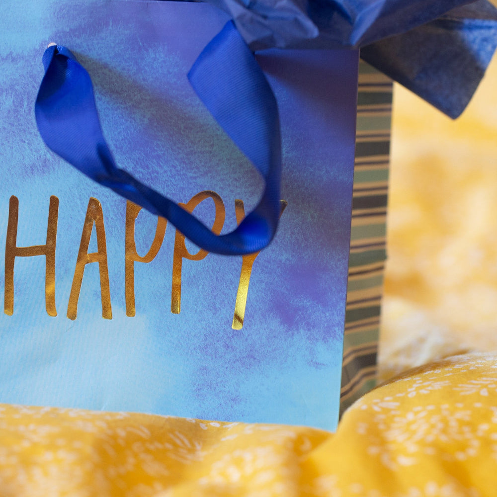 Blue gift bag with 'HAPPY' text and a blue ribbon, partially obscured by yellow fabric.
