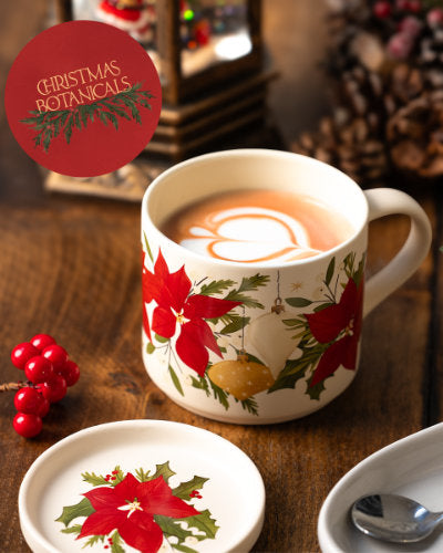 Decorative Christmas-themed mug and matching coaster with a floral design on a wooden surface with berries and acorns.