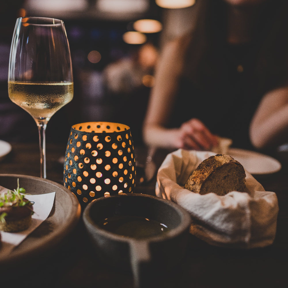 Glass of white wine, bread basket, and candle on a table with blurred background