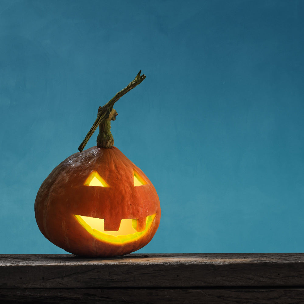 Carved pumpkin with a glowing face on a wooden surface against a blue background