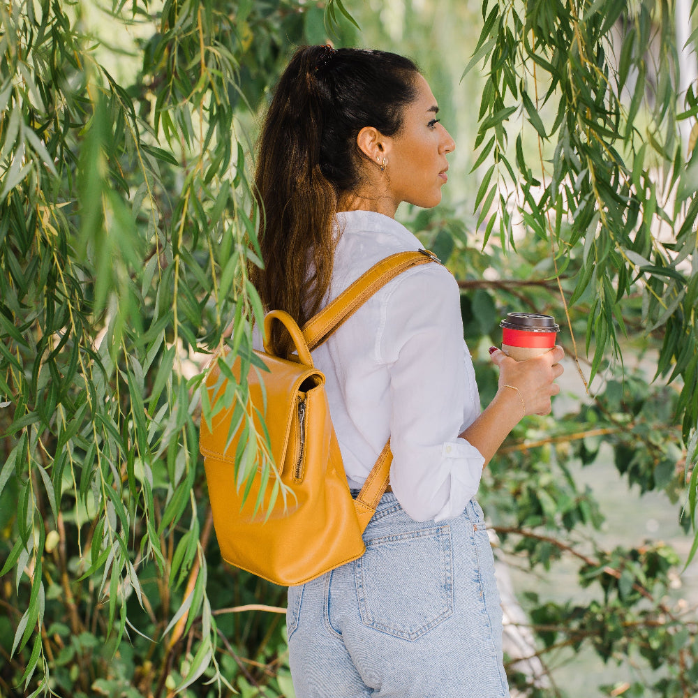 Woman with a yellow backpack and red cup standing among green foliage