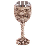 Angled view of a bone-coloured decorative goblet, featuring a bowl and base covered in multiple skulls, a spine-shaped stem, and a silver-coloured metallic rim.