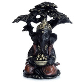 Front view of a black and gold Ganesh figurine sitting under a tree, holding a bowl of gold items.