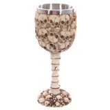 Full view of a decorative bone-coloured multi-skull and spine goblet, featuring numerous skull designs on the bowl and base, a spine-like stem, and a metallic silver-coloured inner rim.