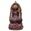 Front view of a dark brown, textured skull crystal cave backflow incense burner, with a skull peering over a glittery purple and pink interior featuring clear crystals. It has bone-like detailing at the base and a brown incense cone at the top.