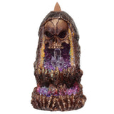 Front view of a dark brown, textured skull crystal cave backflow incense burner, with a skull peering over a glittery purple and pink interior featuring clear crystals. It has bone-like detailing at the base and a brown incense cone at the top.