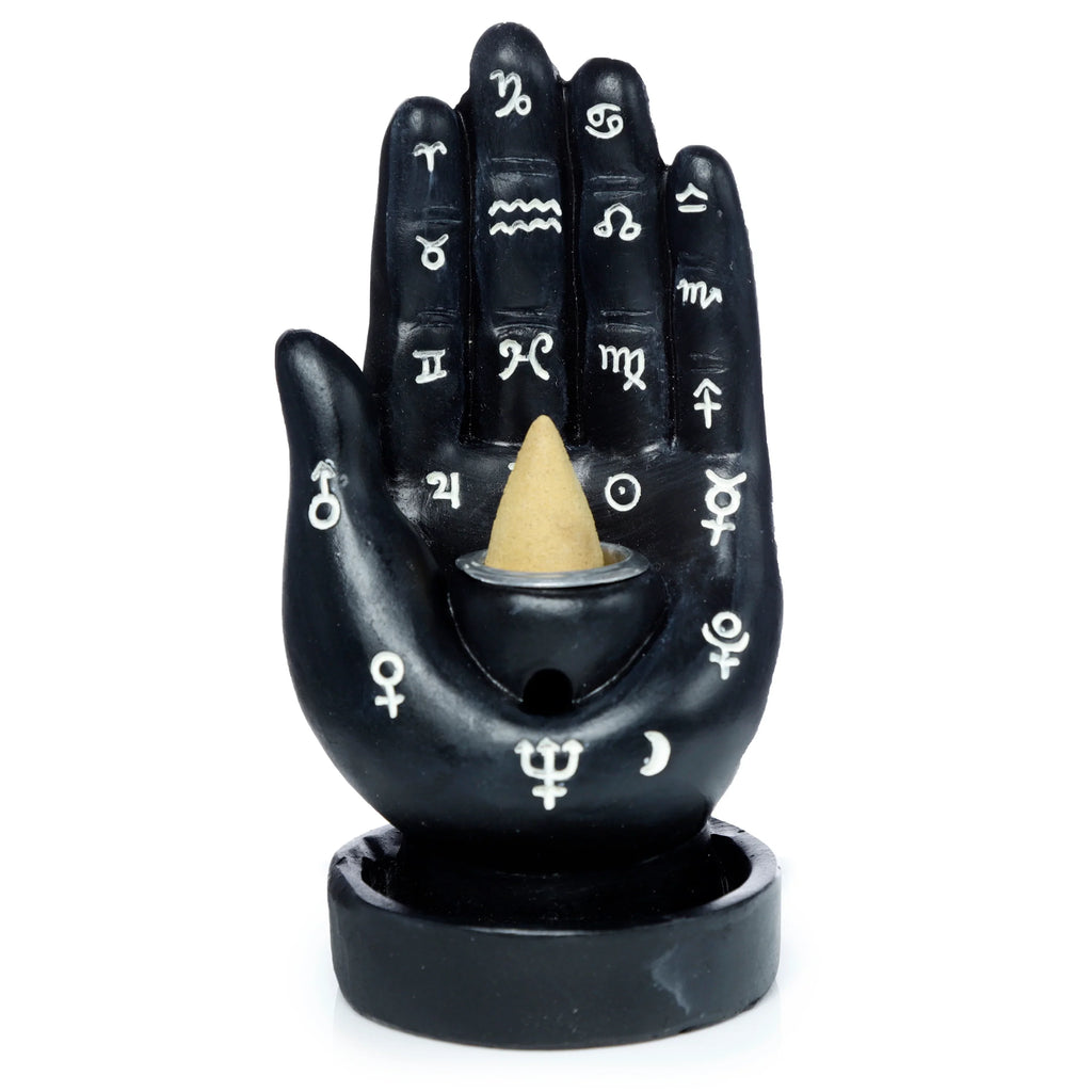 Front view of a black hand-shaped backflow incense burner, decorated with white astrological symbols, holding a light-coloured incense cone.