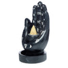 Angled view of a black hand-shaped backflow incense burner, adorned with white celestial and zodiac symbols on the palm and fingers, holding a light brown conical incense cone in a silver-coloured holder, atop a black circular base.