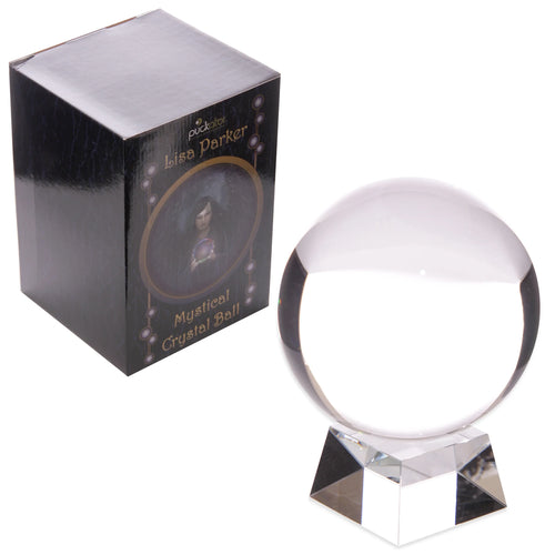 Angled view of a clear spherical crystal ball resting on a faceted glass stand, positioned beside a dark gift box depicting a woman holding a sphere.
