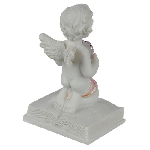 Rear angled view of a white cherub figurine with textured wings, kneeling on an open book. The cherub holds a pink crystal heart, with pink glitter detail visible on its lower back.