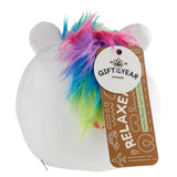 Angled view of a white round plush unicorn travel pillow, featuring soft multi-coloured (pink, purple, blue, green) faux fur for its mane and two small ears. An attached product tag displays 'Relaxeazzz Travel Pillow with Eye Mask' and 'Gift of the Year Winner'.