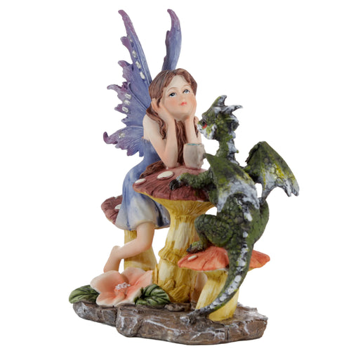 Front view of a Woodland Spirit Fairy figurine, depicting a fairy with purple wings and a blue dress leaning on a mushroom, sharing a tea party with a green dragon holding a mug. A pink flower is visible on the rocky base.