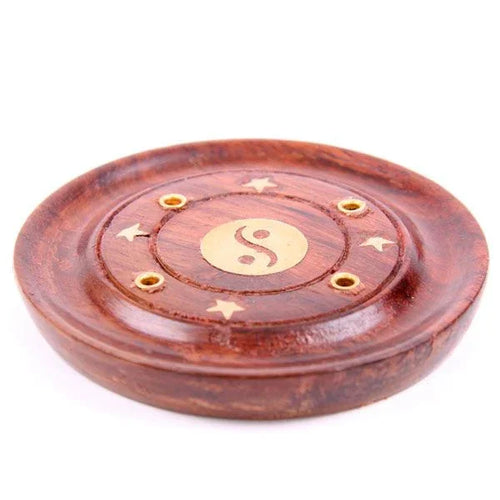 Angled view of a round reddish-brown wooden incense holder and ashcatcher, featuring a brass-coloured Yin Yang inlay in the centre, surrounded by five circular incense stick holders and four star-shaped inlays.