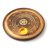 Angled view of a round dark mango wood incense ashcatcher, detailed with a golden pentagram, concentric rings, multiple stick holes, and a cone burner cup.