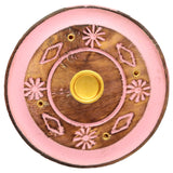 Overhead view of a round mango wood ashcatcher incense holder. It features a pink coloured outer ring and intricate pink floral and diamond patterns on the natural wood centre, with a central brass cone burner and four brass incense stick holes.
