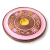 Angled top view of a round mango wood incense holder, featuring a pink painted floral and diamond design. This ashcatcher has a central gold-coloured cone burner and small holes for incense sticks.