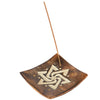 Angled top-down view of a square mango wood incense stick burner, functioning as an ashcatcher, with a light carved geometric star pattern and small brass-coloured studs. A brown incense stick is inserted into the holder.