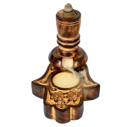 Angled view of a dark mango wood backflow incense burner, featuring a Hamsa hand base with intricate carved floral patterns, smoke flowing from the burning cone.