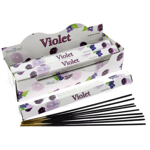 Angled view showing a white cardboard display box containing several purple 'Violet' incense stick packets, with one packet and loose black incense sticks with golden tips visible in the foreground.