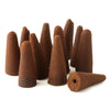 Angled view of multiple dark brown conical backflow incense cones, some standing upright, with one cone lying on its side clearly showing its central base hole, all on a white background.