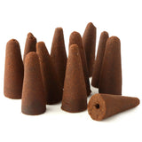 Close-up of several dark brown, conical backflow incense cones. One cone is lying on its side, clearly showing the hole in its base.