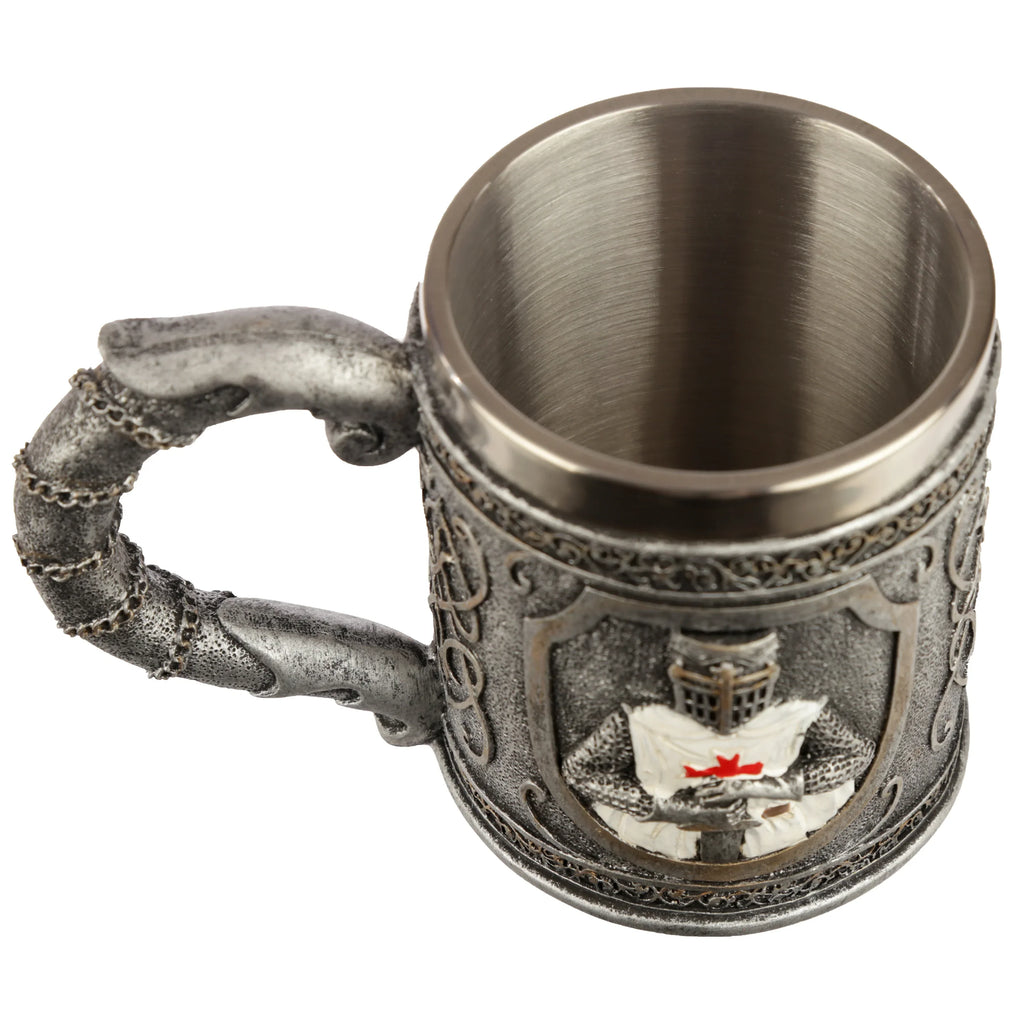 Overhead angled view of a decorative Crusader Knight Tankard, featuring a metallic grey finish, an intricate handle with textured chain details, and a central embossed shield motif depicting a knight in armour with a red cross. The tankard's brushed metal interior is visible.