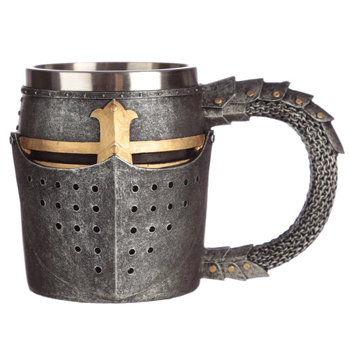 Angled view of a decorative tankard shaped like a medieval helmet, featuring a textured grey finish, gold-coloured visor and cross detailing, circular ventilation holes, and a distinctive chain mail handle, on a white background.