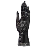 Small black and white mantric hand ornament, front view, intricately detailed with white mystical symbols including a prominent eye, stars, a coiled snake, and geometric patterns.