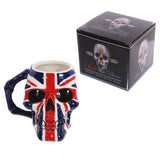 Front-angled view of a ceramic UK Flag Skull Head mug, depicting a Union Jack design in red, white, and blue, with a bone-shaped handle.