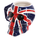 Angled view of a ceramic skull head mug, decorated with a red, white, and blue UK Flag design, showing black eye sockets and a sculpted blue handle.
