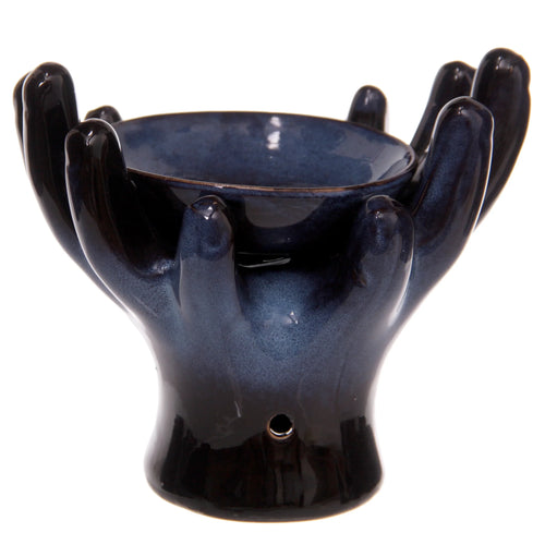 Angled view of a dark blue, mottled, glazed ceramic oil burner, shaped as open hands cradling a central bowl, with a candle hole visible near the base.
