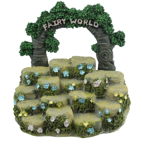 Front view of a Fairy World Figures Display Stand, featuring tiered rock-like levels adorned with green foliage and colourful blue, yellow, and pale pink flowers. An archway of leafy tree trunks spans the top, displaying the words 'FAIRY WORLD'.
