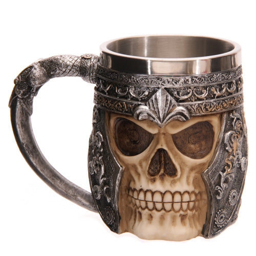 Front angled view of a decorative skull warrior tankard, displaying a light-coloured skull with dark eye sockets, wearing an ornate, dark silver-coloured warrior helmet detailed with bronze-coloured scrollwork and a prominent central crest. The tankard has a plain silver-coloured metal interior liner and a textured, dark silver-coloured handle.
