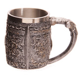 Angled view of a decorative warrior tankard, showcasing its antiqued silver-grey finish with intricate raised scrollwork, a textured, armour-like body, and an ornate handle.
