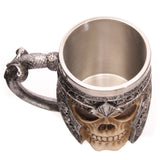 Angled top-down view of a decorative skull warrior tankard, showing its bone-coloured skull design, metallic grey armour with intricate patterns, textured handle, and a silver-coloured metal interior.