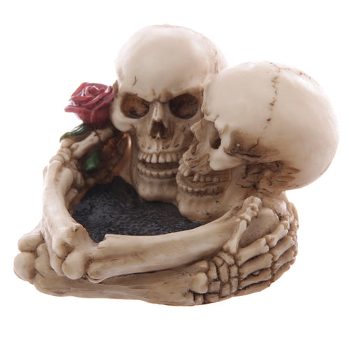 Angled view of a beige skull lovers ashtray, depicting two skulls embracing with a red rose detail and a dark, textured bowl.