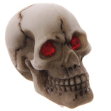 Angled view of a gruesome skull figurine, off-white with brown crack detailing and sparkling red gem eyes.