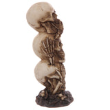 Hear No Speak No See No Evil skull totem ornament, side profile view, with three stacked cream-coloured skulls showing bone details and dark accents, resting on a textured dark brown base.