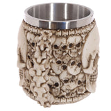 Angled view of a decorative multi-skull tankard, showcasing its cream-coloured exterior with embossed skulls, a sculpted bone-effect handle, and a polished metal interior.