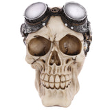Front view of a steampunk style skull decoration, an off-white figurine with an aged appearance, wearing metallic silver goggles with dark brown frames and intricate gear details.