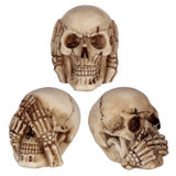 Set of three small beige resin skull ornaments. The top skull is shown from the front, with skeletal hands covering its eyes ('see no evil'). Below, two skulls are angled, one with hands covering its mouth ('speak no evil') and the other with hands covering its ears ('hear no evil'). All skulls feature a weathered, bone-like appearance.