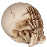 Close-up of a bone-coloured 'See No Evil' skull ornament, featuring dark, aged detailing and skeletal hands covering its eyes.